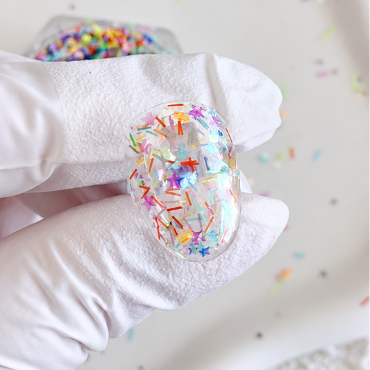 Gloved hand displaying a nail swatch encapsulated with Sugar Rush colorful sprinkle and star glitter mix.
