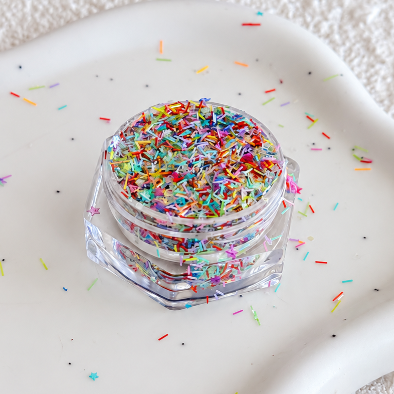 Open clear jar of Sugar Rush colorful sprinkle glitter mix resting on a scalloped ceramic dish.