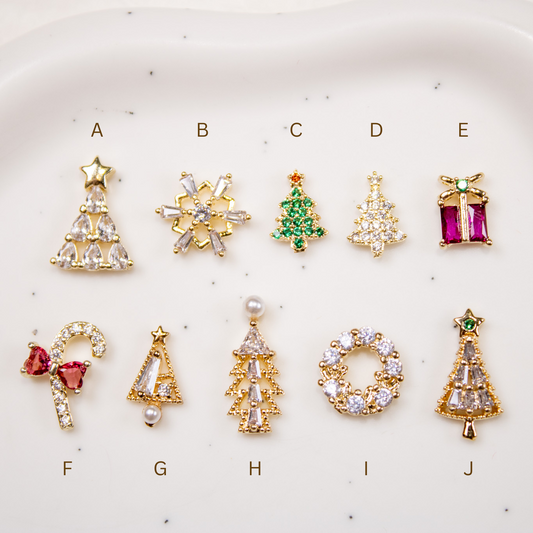 Row layout of various gold and enamel holiday nail charms against a white background.
