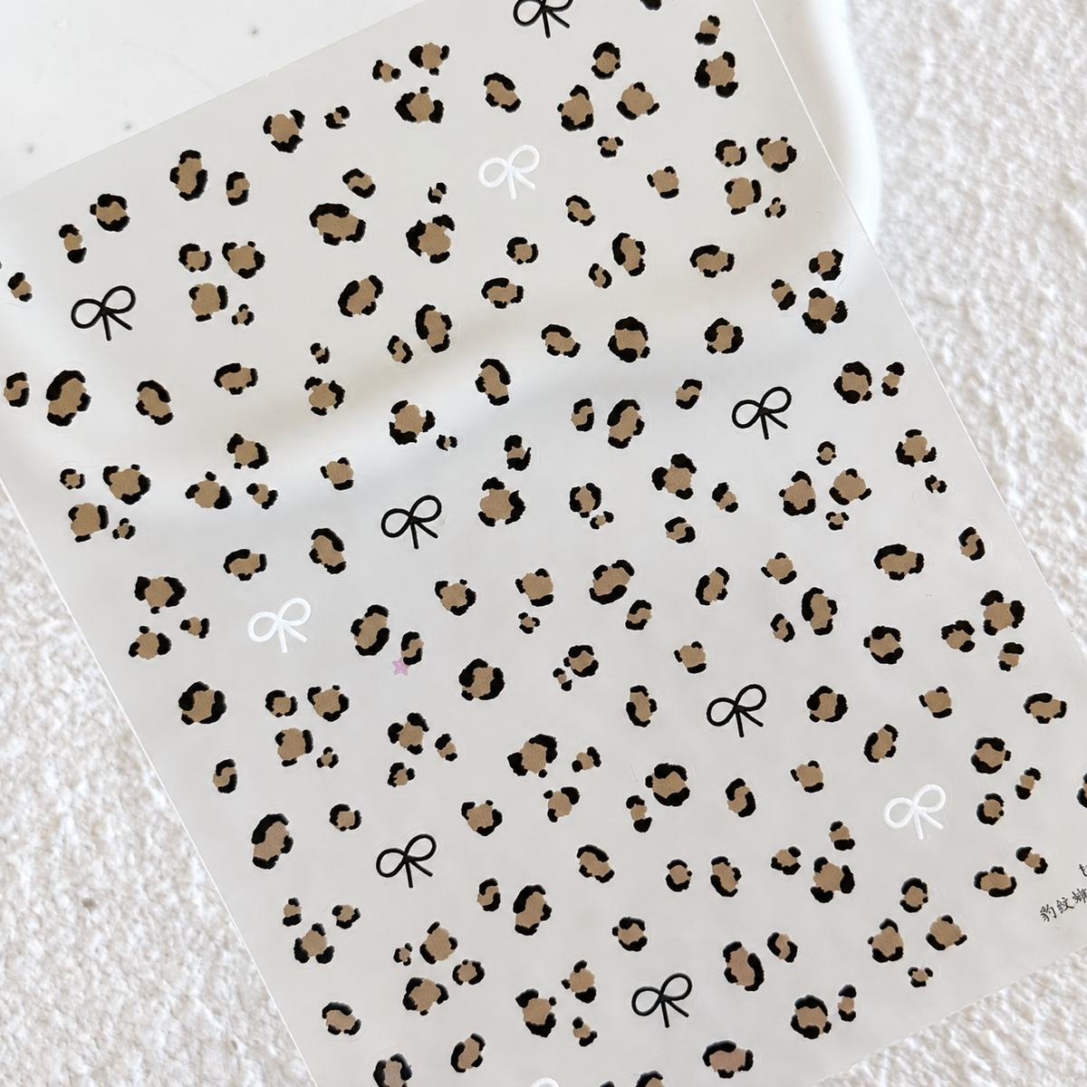 Top-down view of the entire sheet of leopard spots and black and white mini bow nail art stickers.