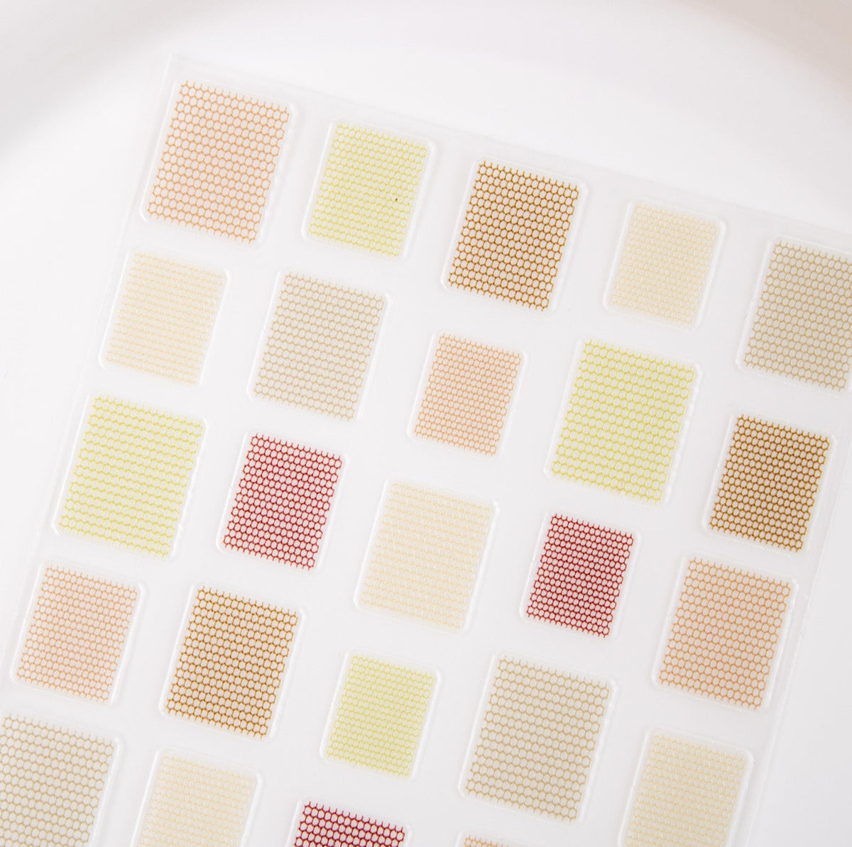 Neutral-toned mesh grid nail sticker sheet with beige, olive, and cream squares on a white dish.