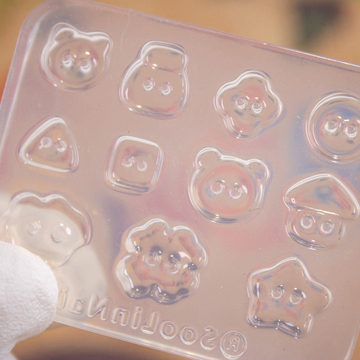 Clear silicone kawaii button mold displayed on a patterned surface showing all design cavities.