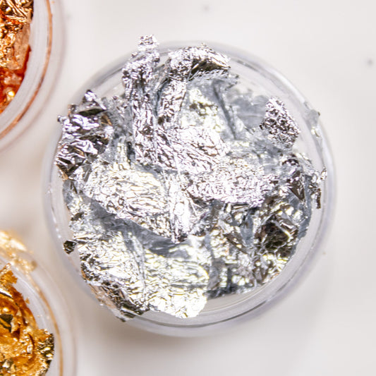Close-up view of silver metallic nail foil flakes in a small clear container.