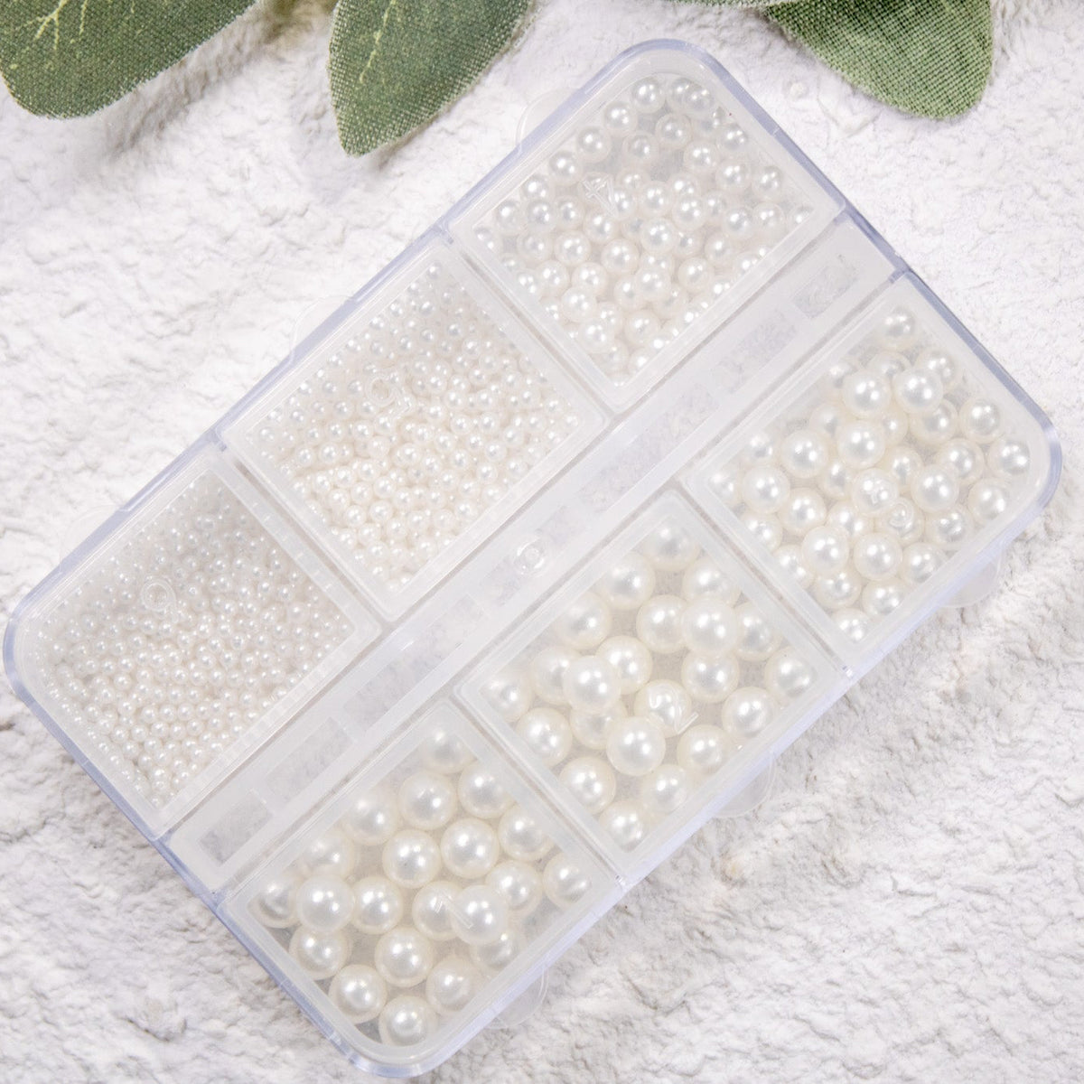 Clear grid storage case filled with various sizes of cream round pearls.