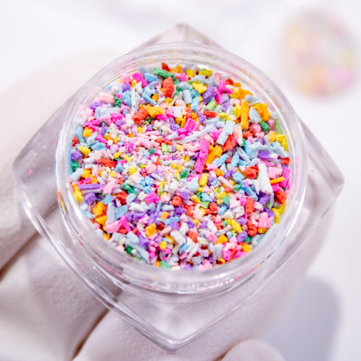 Close-up angled view of an open jar overflowing with colorful nail sprinkles.