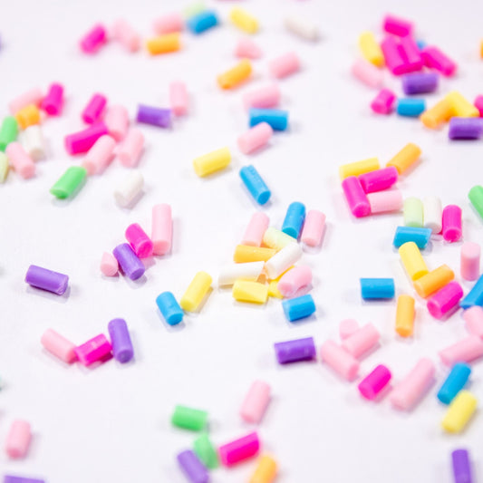Colorful rainbow sprinkle nail art pieces scattered across a white background.