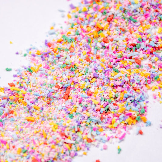 Colorful rainbow sprinkle nail art pieces scattered across a white background.