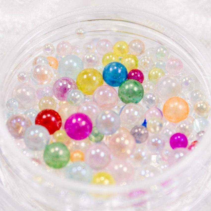 Close-up angled view of a clear square jar filled with colorful jelly drop beads.