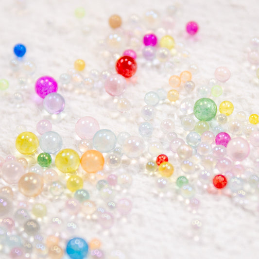 Translucent rainbow jelly drop beads scattered across a clean white surface.