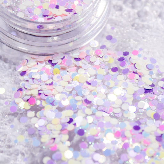 Iridescent pastel circle confetti glitter scattered across a textured surface.