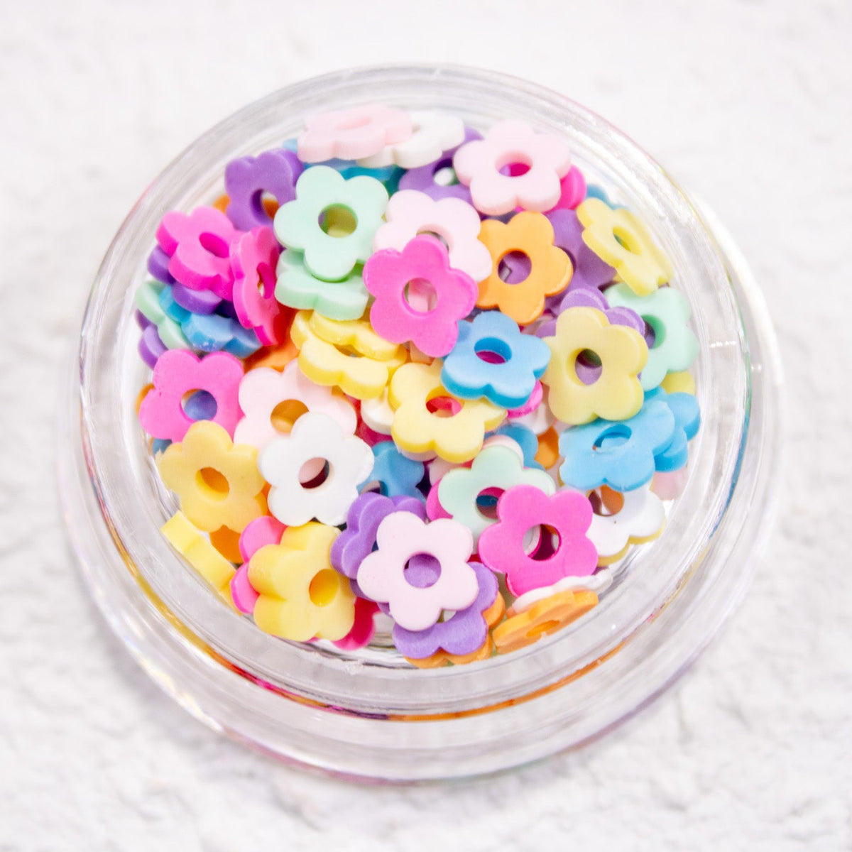 Close-up view of a clear round jar filled with 30 pieces of pastel flower nail charms.