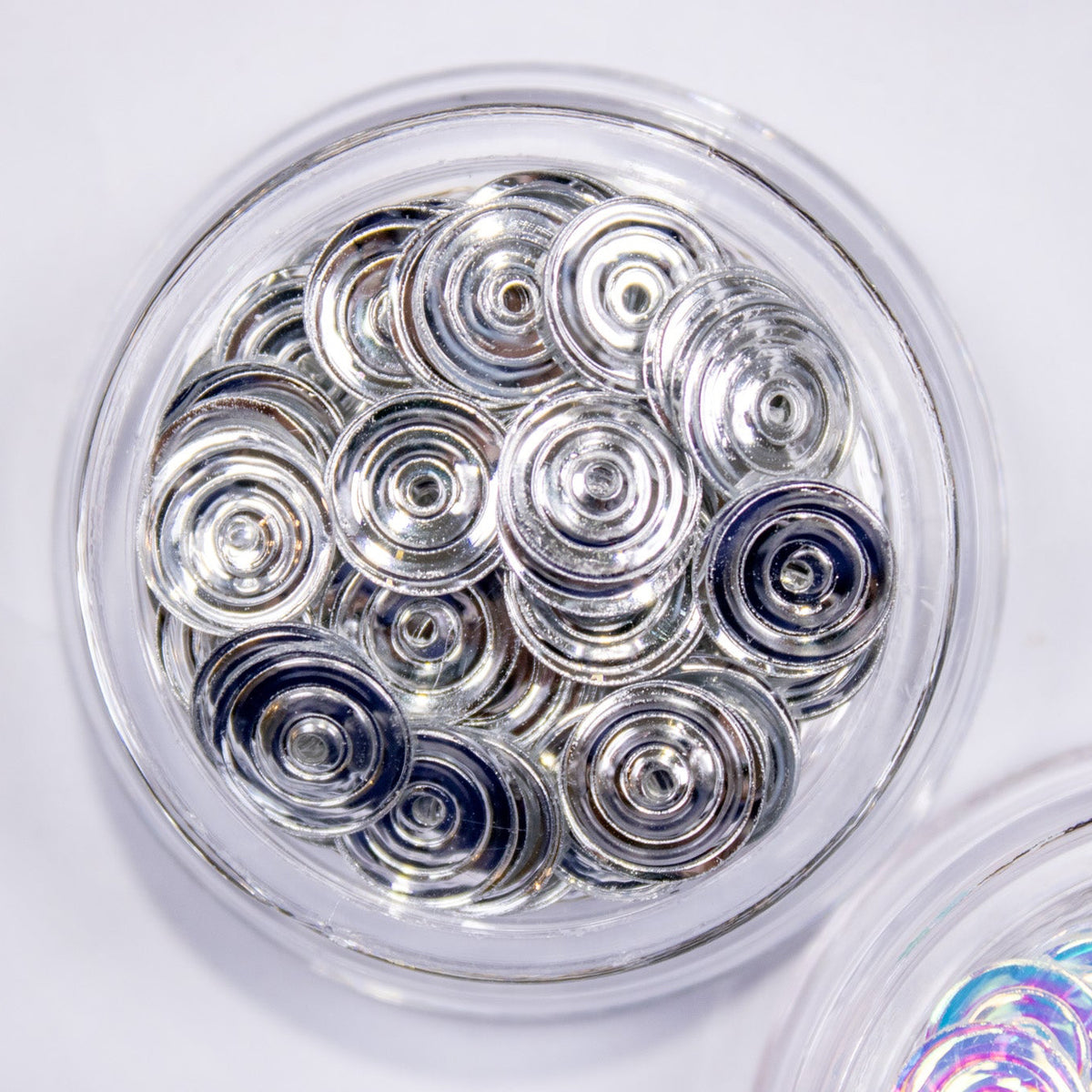 Clear round jar packed with metallic silver disco swirl nail charms.