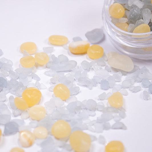 Pastel yellow and icy blue pebble stones scattered across a white surface next to a clear jar.
