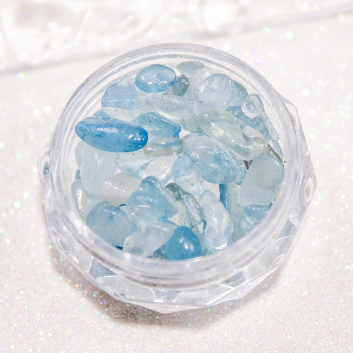 Top-down view of clear round jar filled with icy blue sea-glass pebble nail stones.