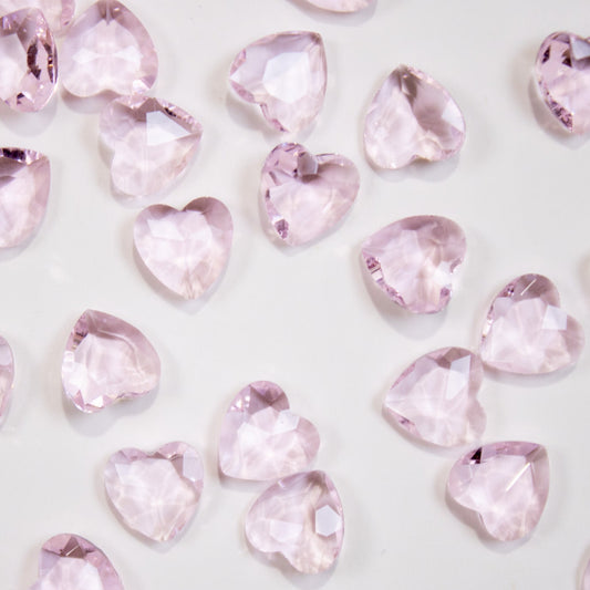 Scattered blush pink heart-shaped faceted crystal nail gems on a clean white surface.