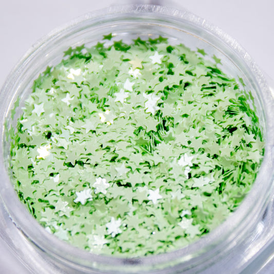 Close-up view of a clear jar filled with green mini star-shaped nail glitter.