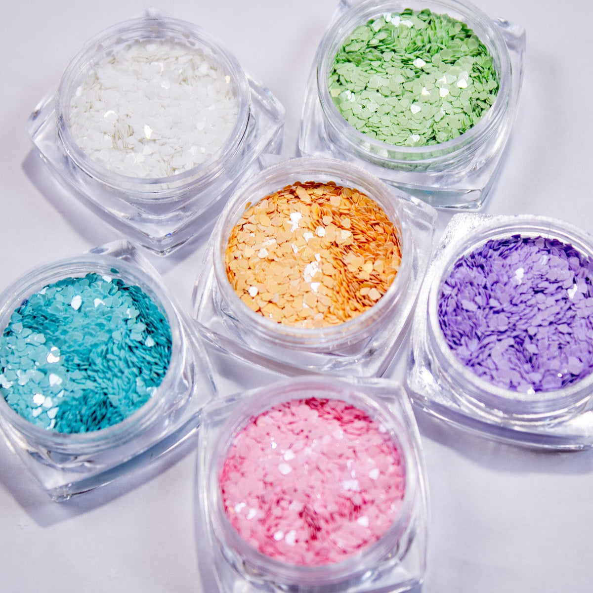 Six small jars of colorful micro heart nail glitter grouped together.