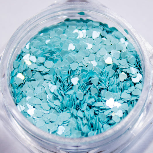 Close-up view of a clear jar filled with light blue mini heart-shaped nail glitter.
