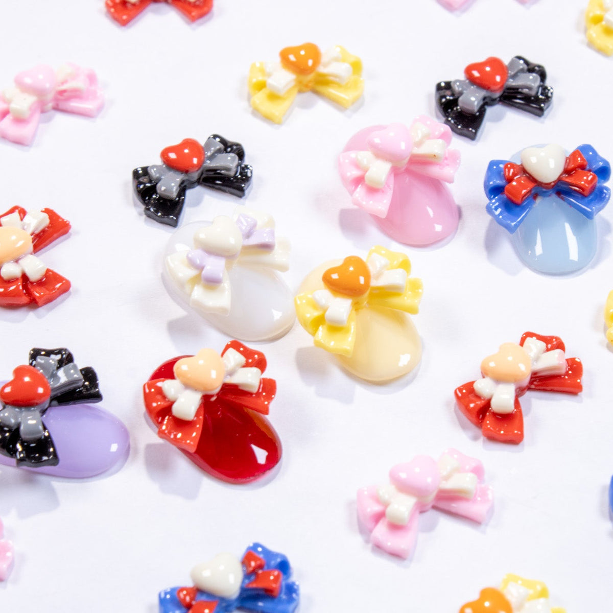 Top-down flat lay of assorted colorful heart bow nail charms in pink, blue, yellow, red, black, and white.