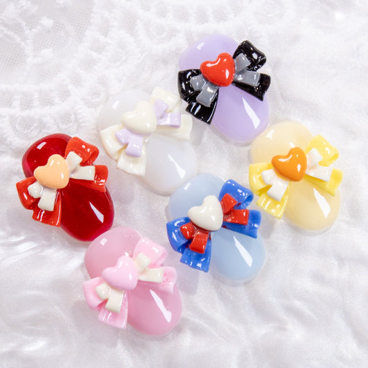 Six colorful heart bow nail charms arranged in a circle on a furry white background.