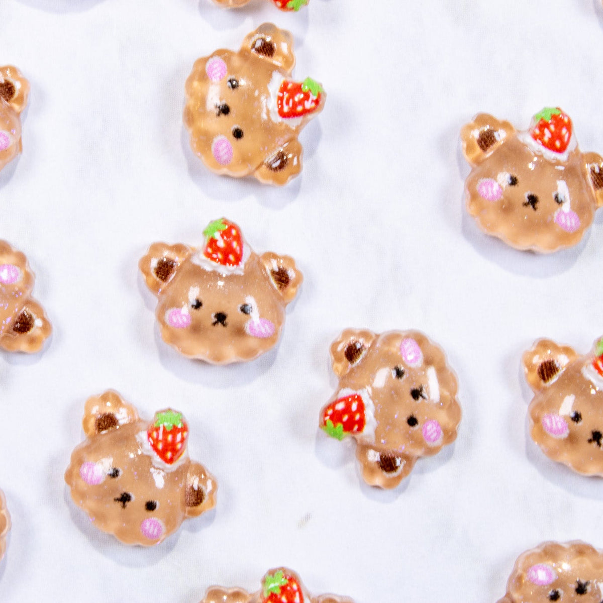Top-down view of miniature strawberry bear pie dessert nail charms scattered on a white background.