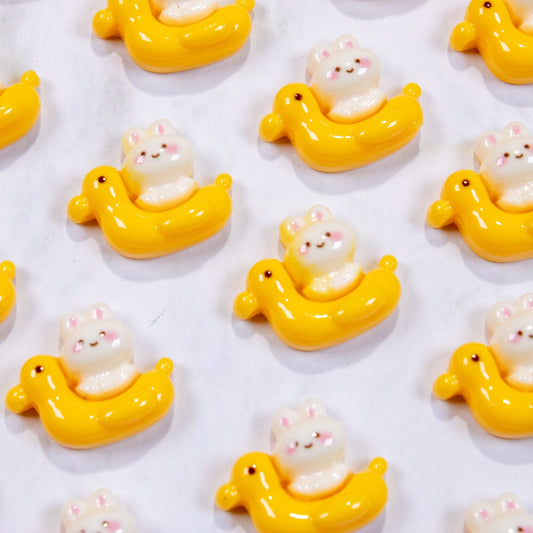 Top-down view of yellow duck floatie bunny nail charms arranged in a grid pattern.