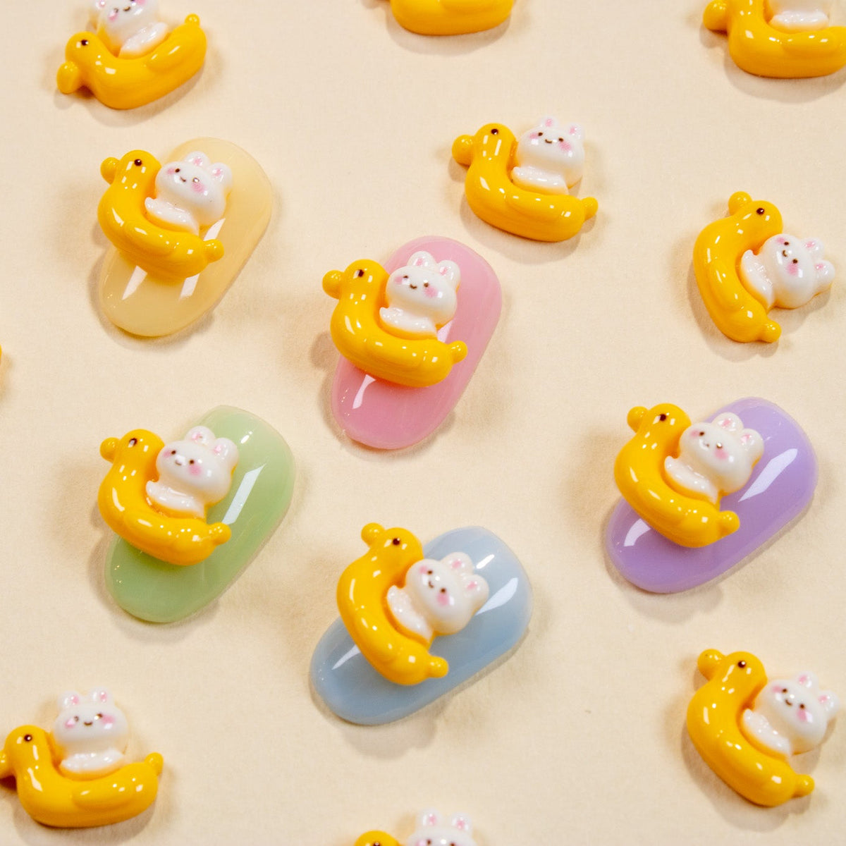 Assorted duck floatie bunny 3D nail charms scattered across a cream background with pastel press-on samples.