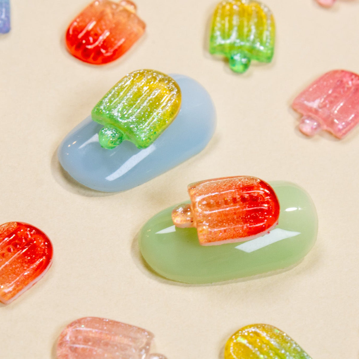 Blue and green press-on nail samples surrounded by scattered colorful mini popsicle 3D nail charms.