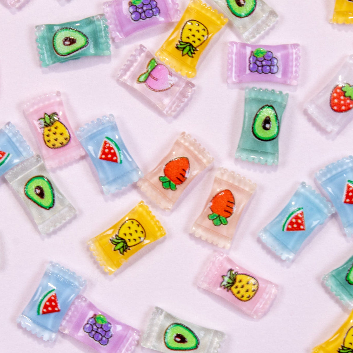 Top-down flat lay of mixed mini wrapped fruit candy 3D nail charms featuring strawberries, avocados, peaches, pineapples, and watermelons.