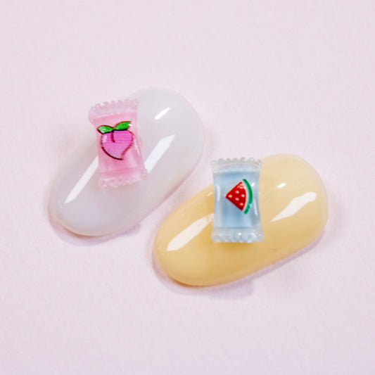 White and pastel yellow press-on nail swatches decorated with peach and watermelon mini fruit candy nail charms.