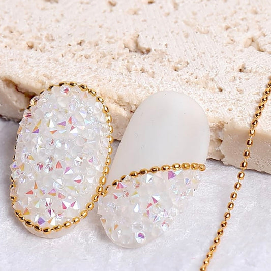 Dainty gold bead chains outlined on a glittery white nail tip.