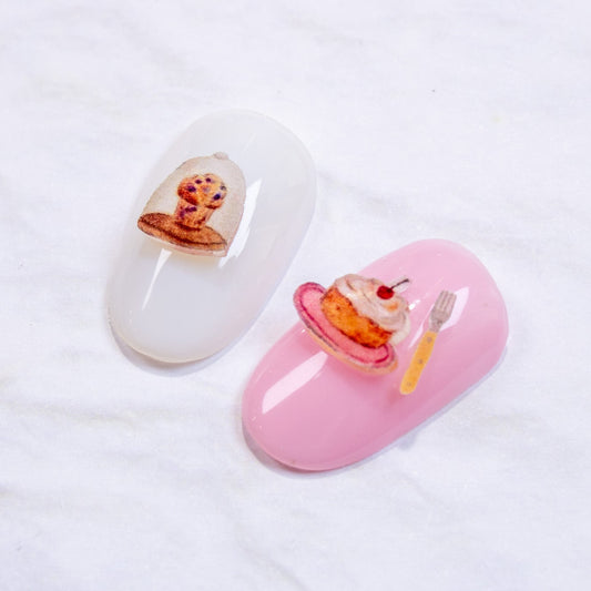 White and pink press-on nail swatches decorated with mini tea-time cake and muffin 3D nail charms.