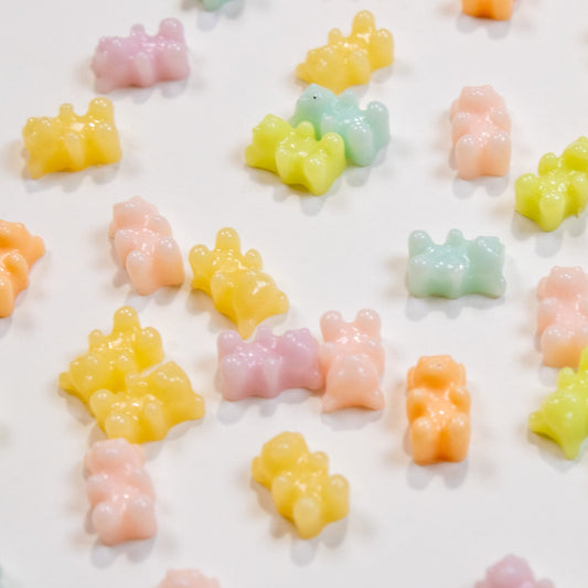 Top-down flat lay of tiny pastel gummy bear 3D nail charms scattered across a white background.