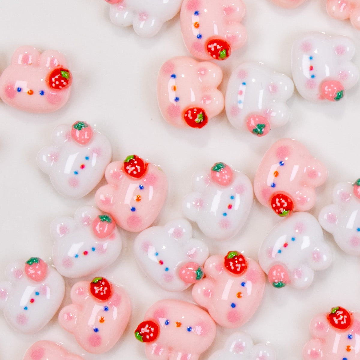 Top-down view of mixed white and pink strawberry bunny 3D nail charms scattered together.