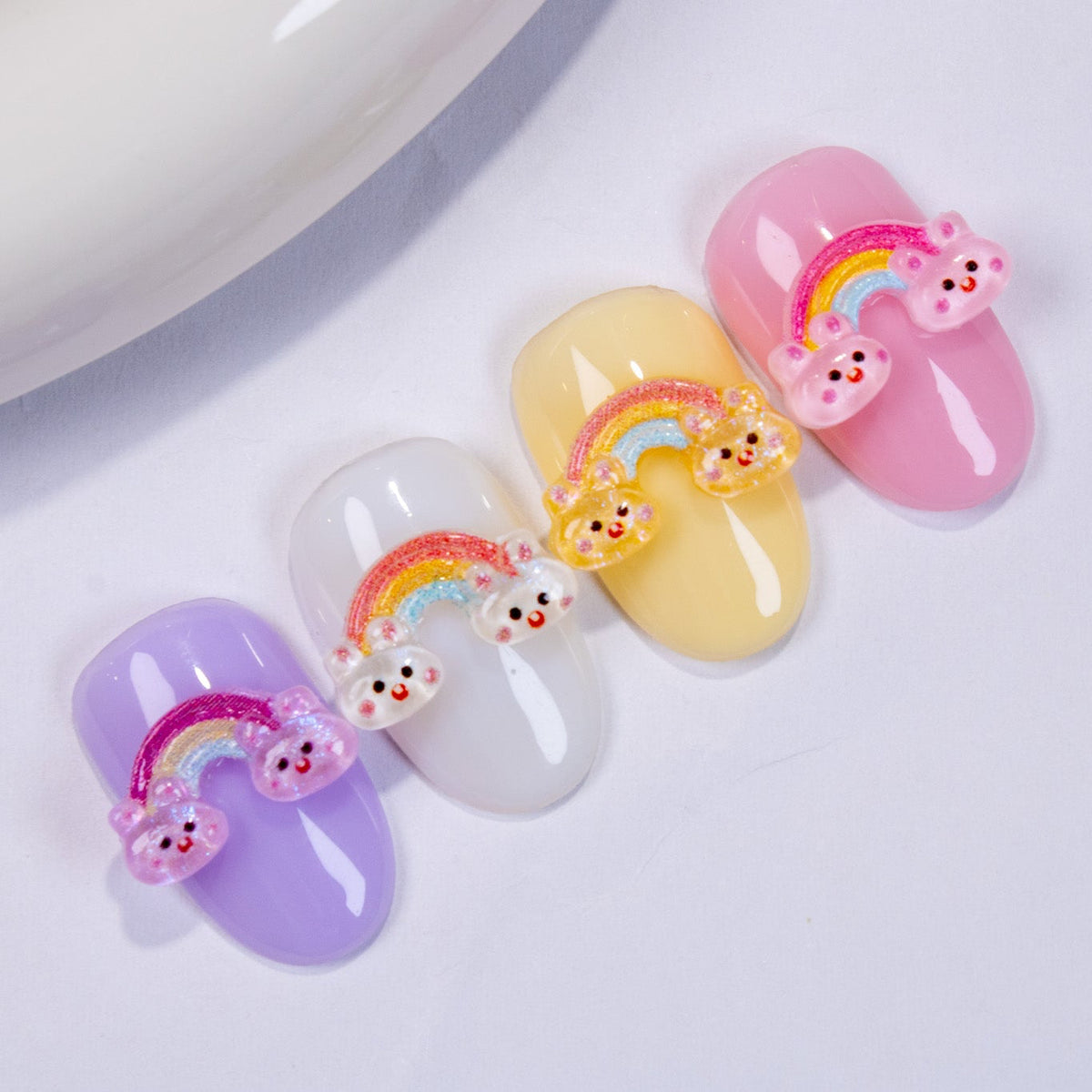 Four press-on nail swatches in purple, white, yellow, and pink, each topped with a matching rainbow bunny 3D charm.