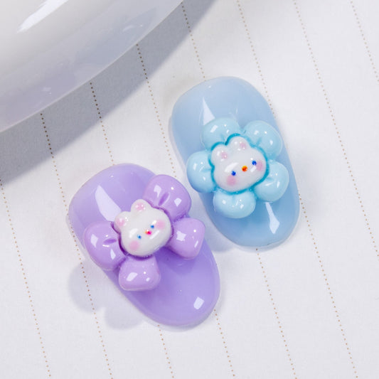 Purple and light blue press-on nail swatches showing a purple bow bunny charm and a blue flower bunny charm on a textured background.