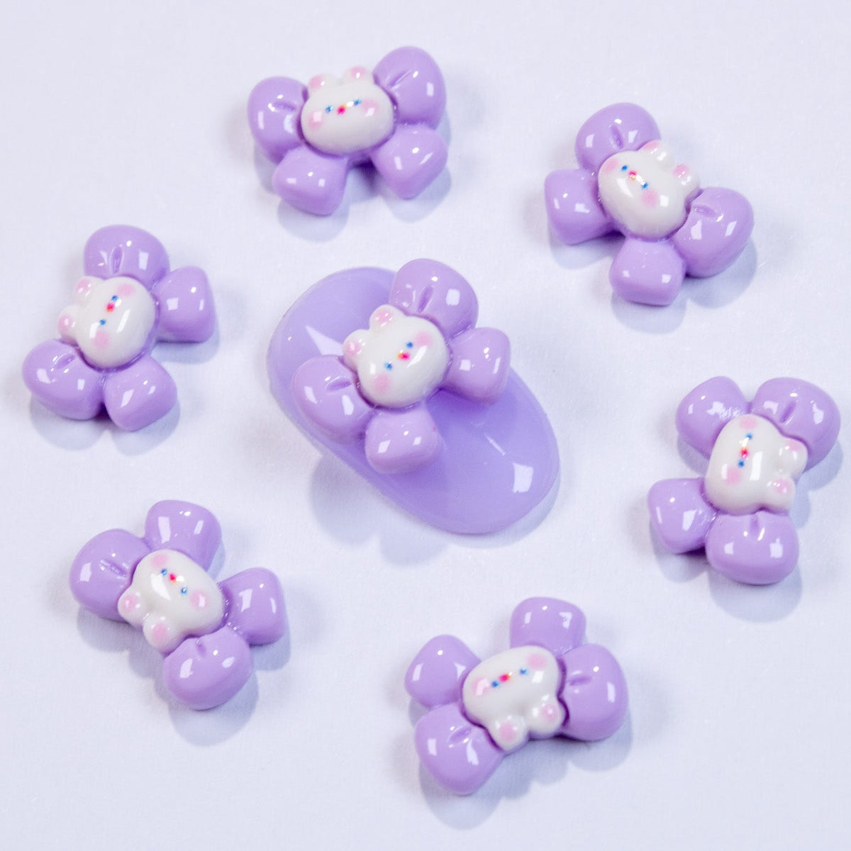 Pastel purple bow bunny 3D nail charms arranged in a ring around a central purple bunny swatch.