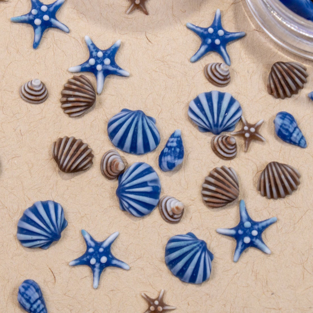 Top-down view of miniature blue and brown starfish, conch shells, and sea charms spread across light beige background.
