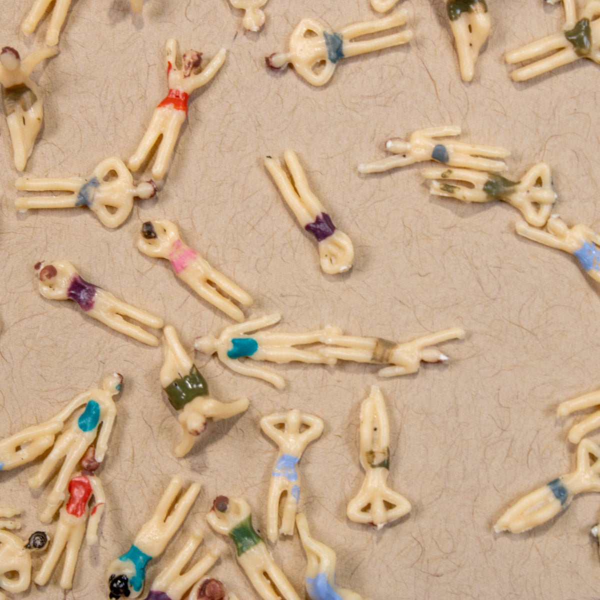 Detailed top-down flat lay pattern of miniature swimmer 3D nail charms in various swimsuit colors.