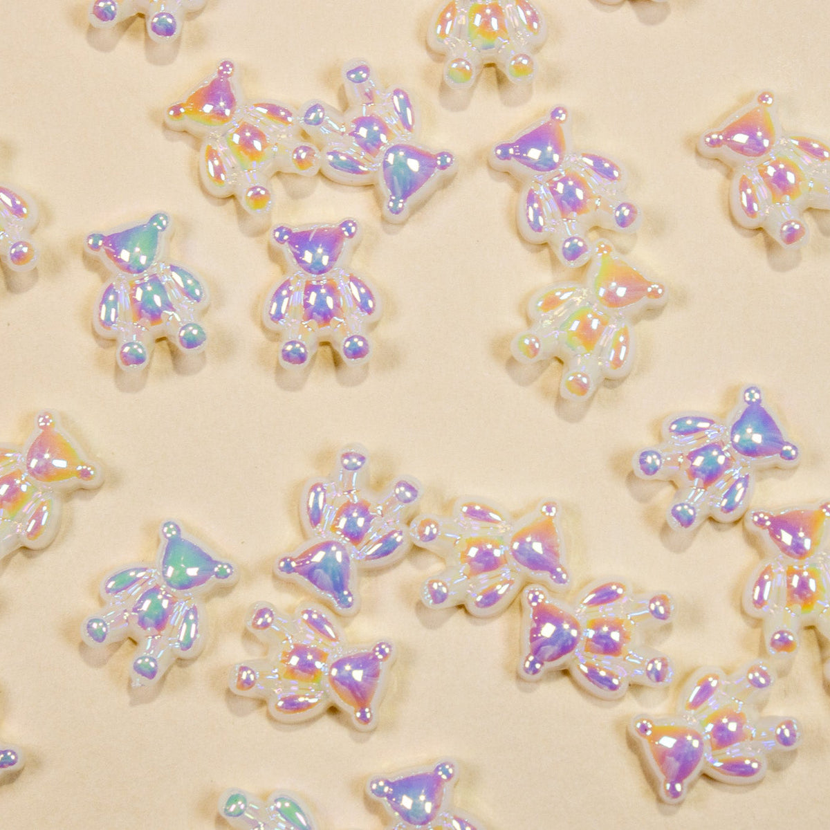 Top-down flat lay pattern of iridescent pearly aurora resin baby bear 3D nail charms on a light yellow background.