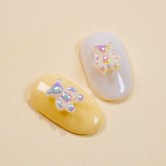 Pastel yellow and white press-on nail swatches showing iridescent pearl baby bear 3D nail charms on a warm neutral background.