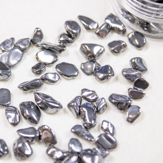Metallic black hematite-style pebble nail stones in organic shapes spilled out onto a light surface.