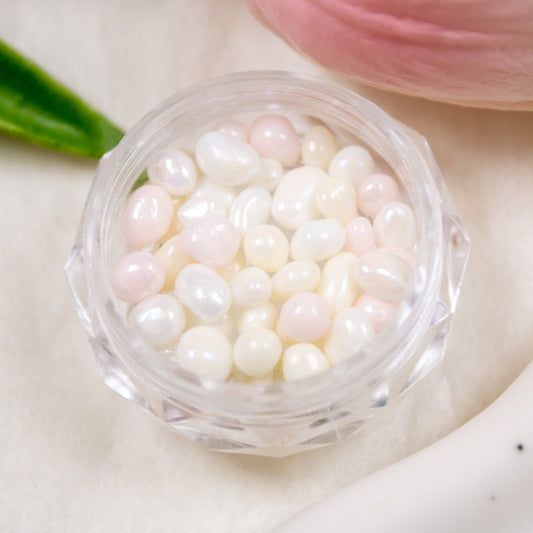 Close-up shot of Cotton Candy jelly pebble nail stones inside an open clear container, featuring pink, ivory, and pearl tones.