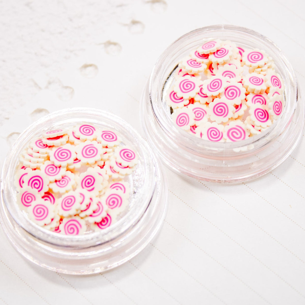 Two open jars filled with pink swirl Narutomaki nail art charms.