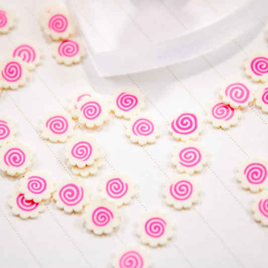Flat lay of scattered Narutomaki swirl nail charms with a jar on a white surface.