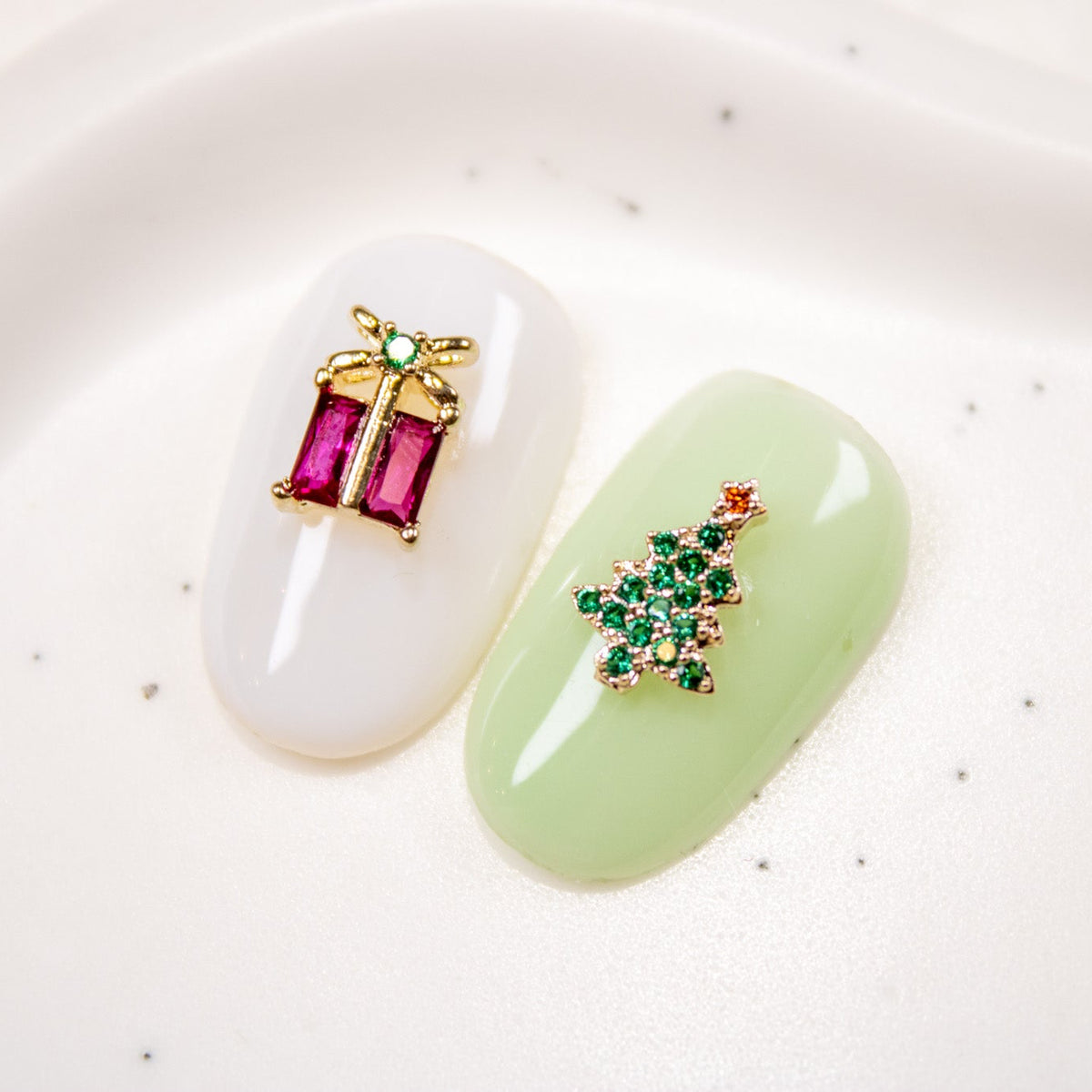 Manicured press-on nails decorated with Christmas tree and gift box nail charm accents.