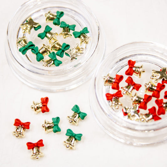 Open jars displaying gold jingle bell nail charms paired with small red and green bow accents.