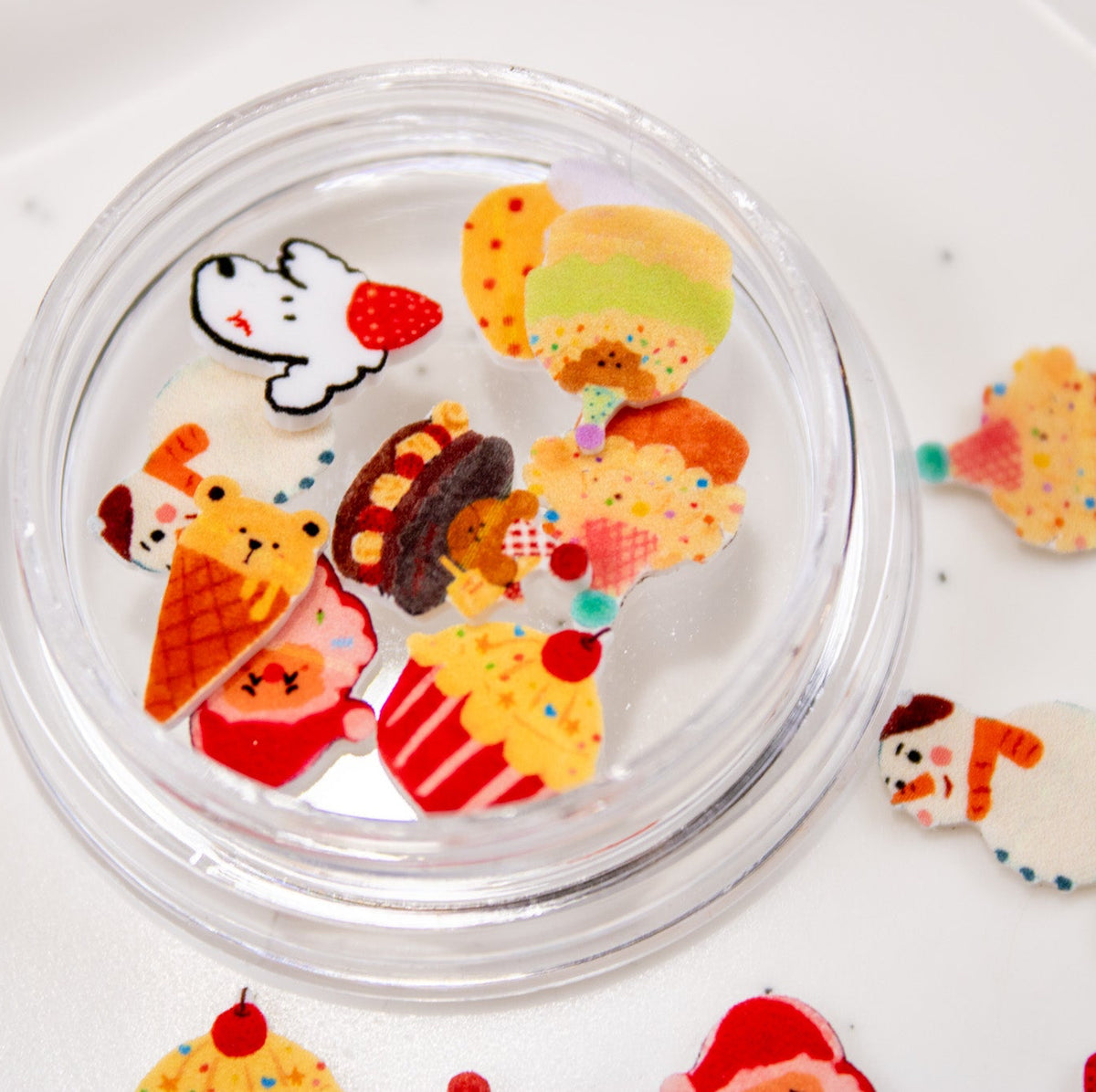 Open jar filled with mixed winter bakery nail charms surrounded by scattered holiday pieces.