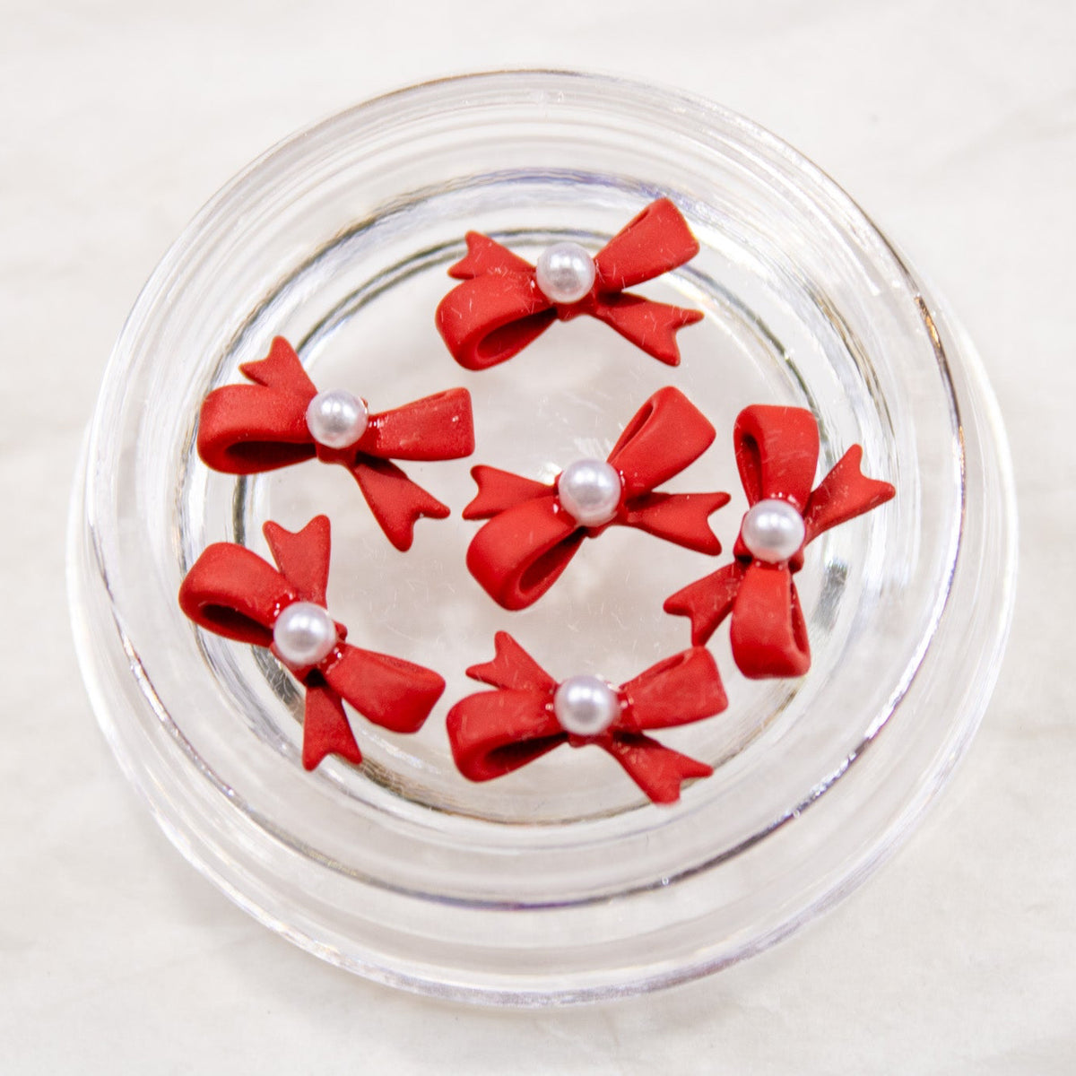 Open jar displaying 3D red pearl bow nail art charms.