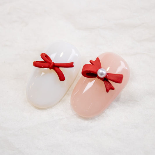 Close-up of false nails decorated with red bow nail charms and pearl accents.
